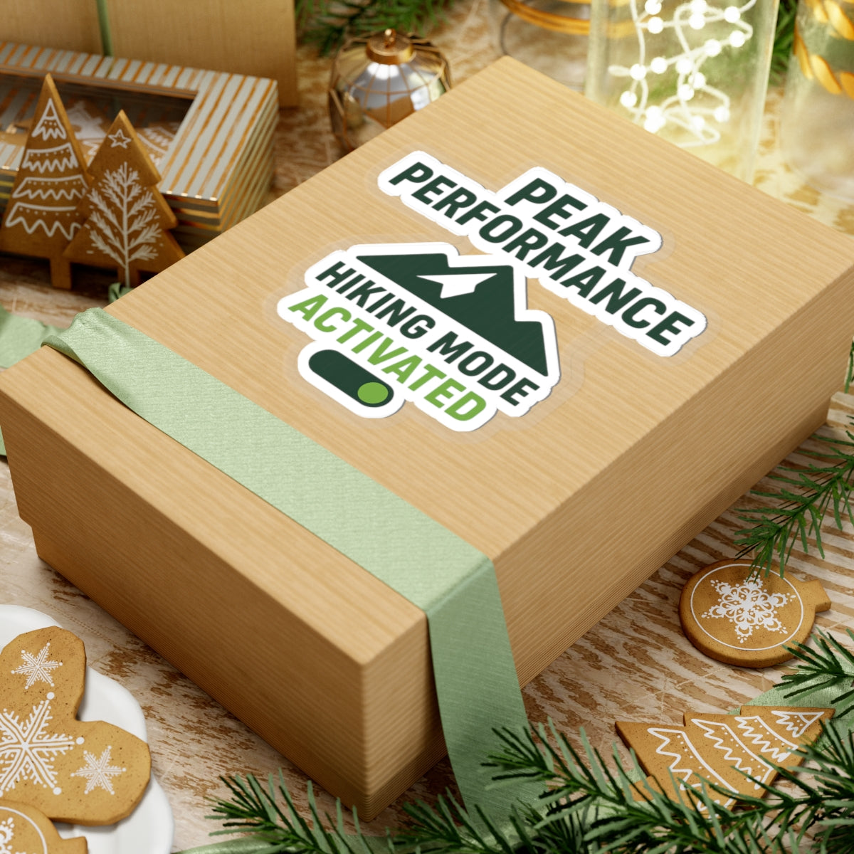 Wooden gift box with a 'Peak Performance Hiking Mode Activated' sticker on a festive background with cookies and decorations.