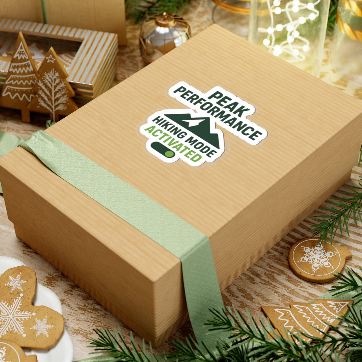 Wooden gift box with green ribbon and 'Peak Performance' sticker on a festive background with cookies and lights.