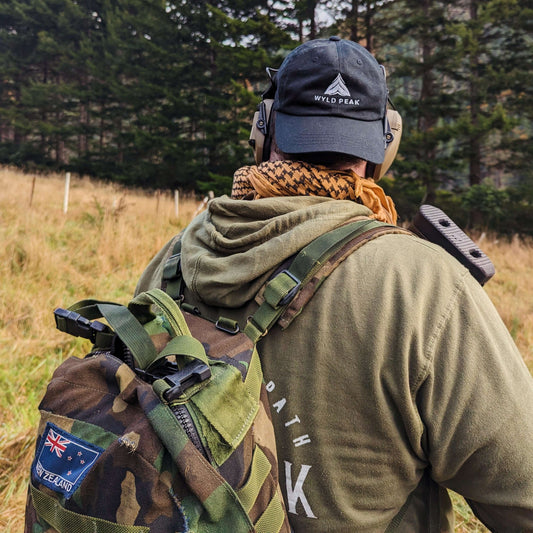 Back view of Hayden wearing a Wyld Peak cap and classic hoodie, holding a long-range rifle while hunting in Marlborough, New Zealand