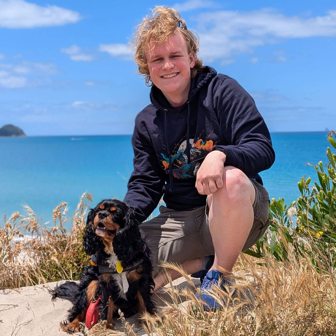Hugo in a Wyld Peak Peak Organic Hoodie with Mellow the King Charles Spaniel, enjoying the coastal views at Marsden Point, New Zealand