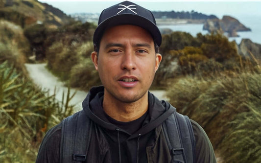 Joe Trinder wearing a cap and Wyld Peak organic hoodie while hiking a scenic New Zealand coastal trail