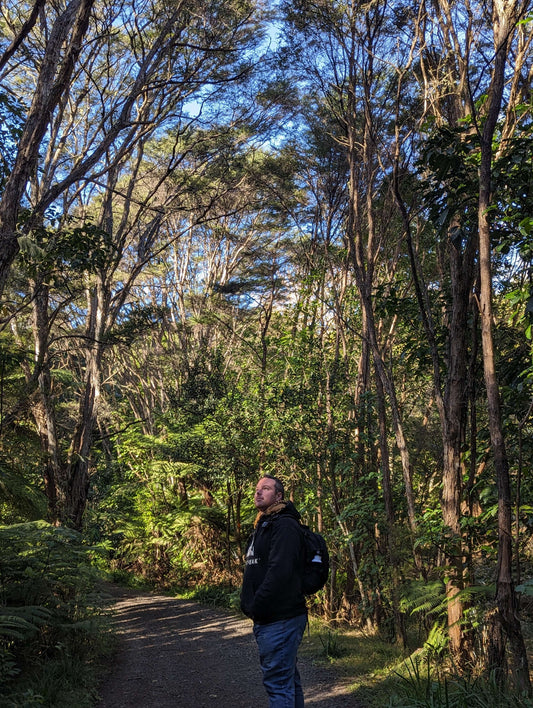 Hayden from Wyld Peak in an organic hoodie standing among native kauri trees and birdsong in New Zealand forest