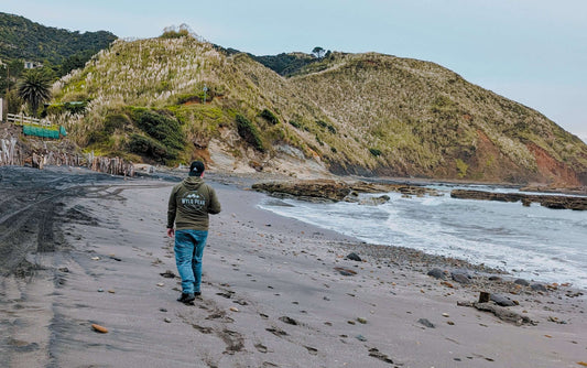 Hayden wearing a Wyld Peak organic hoodie walking along windswept Port Waikato Beach in New Zealand