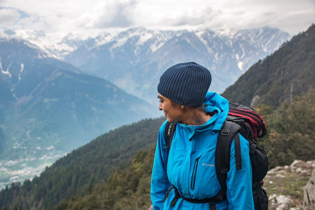 Woman in hiking gear standing on a trail, gazing over a vast scenic valley with layers of hills below