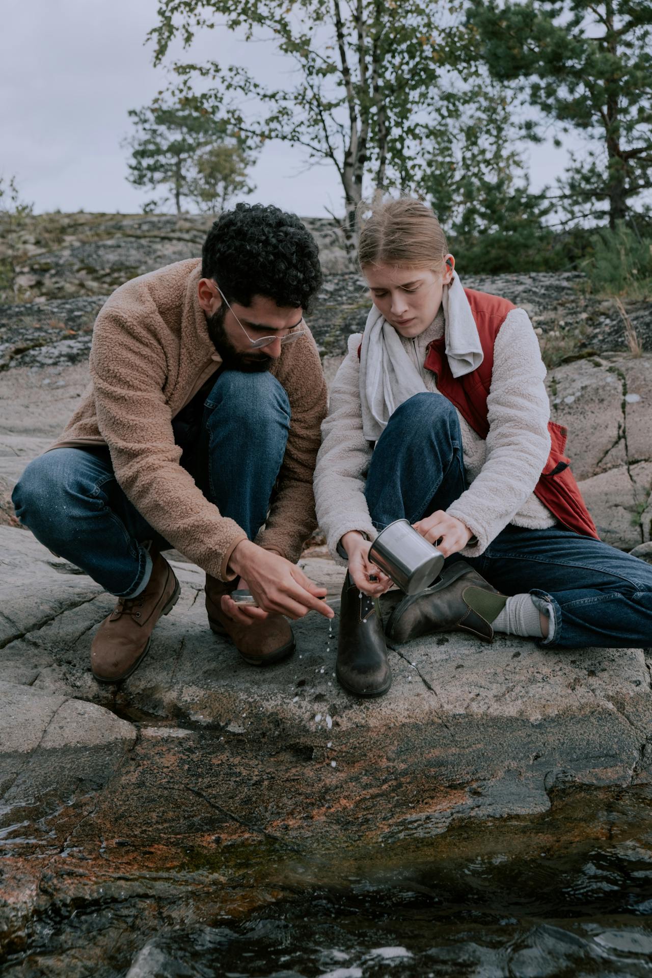 Man and woman pouring fresh water from a river while hiking outdoors