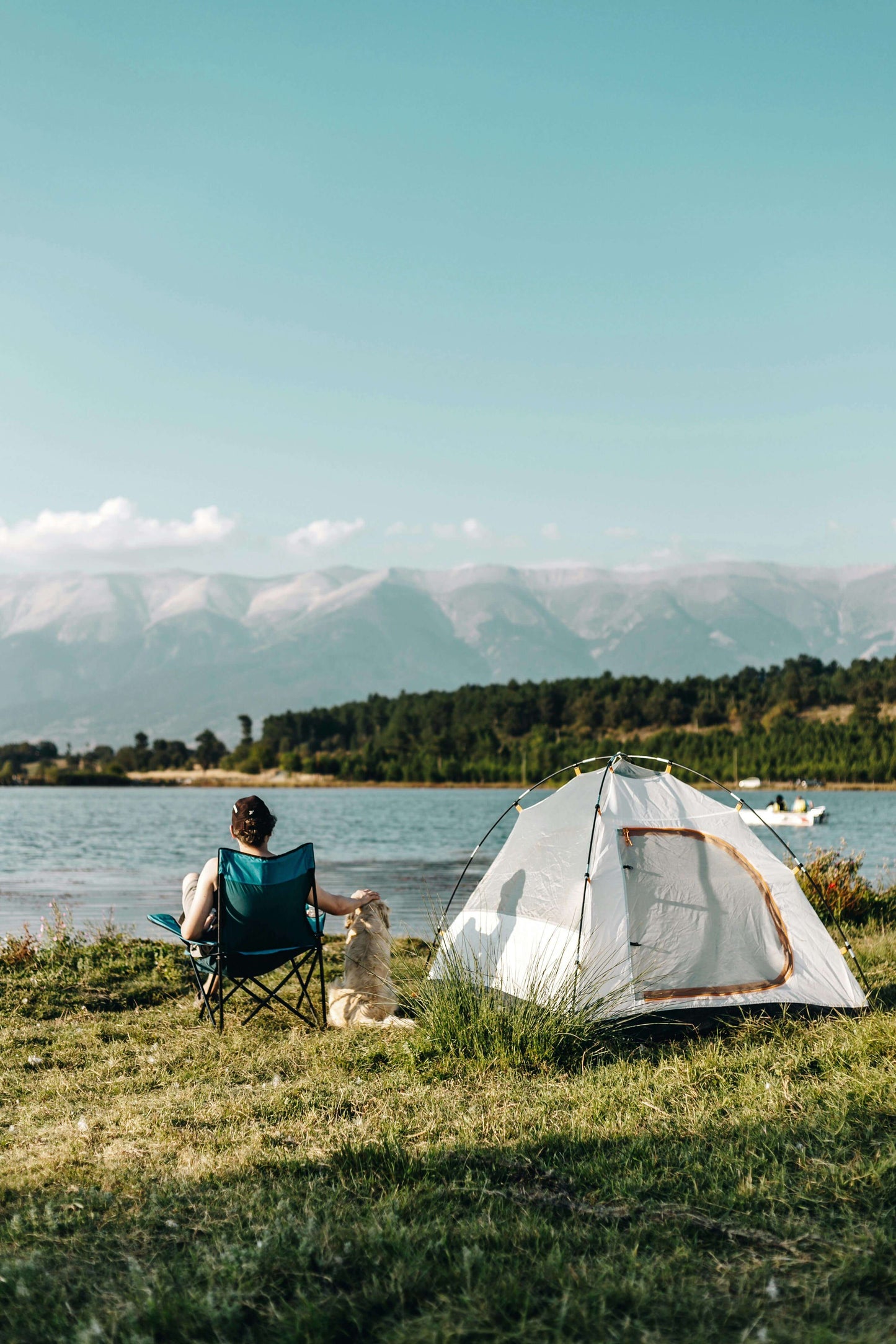 Person with dog at campsite by a mountain lake with tent and campfire.