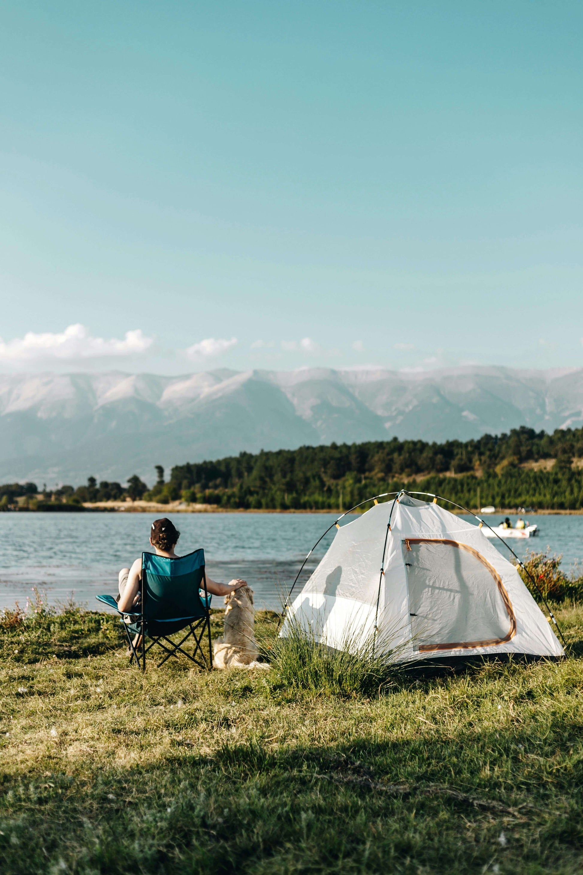 Person with dog at campsite by a mountain lake with tent and campfire.