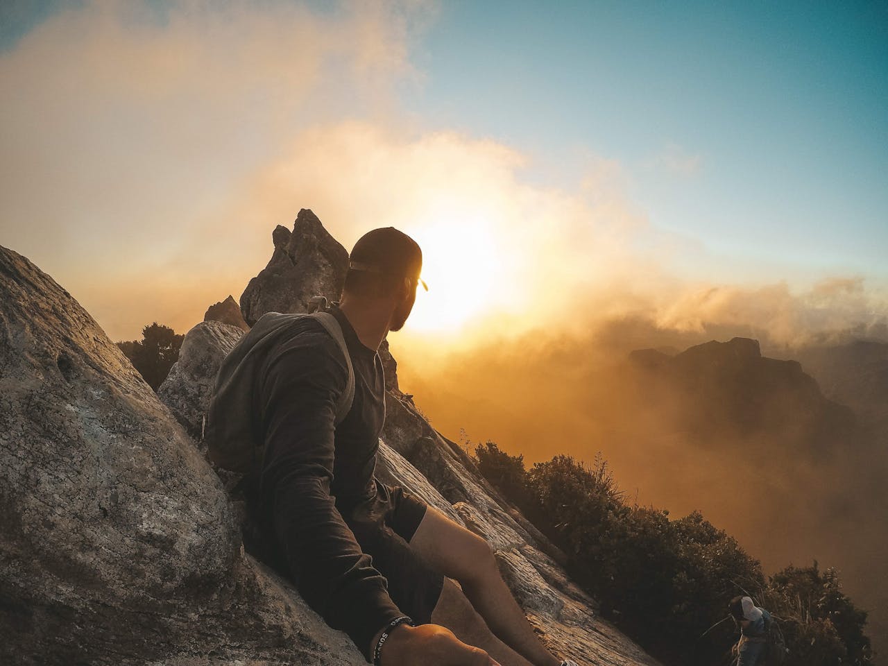 Hiker silhouetted against a vibrant sunset on a mountain peak.