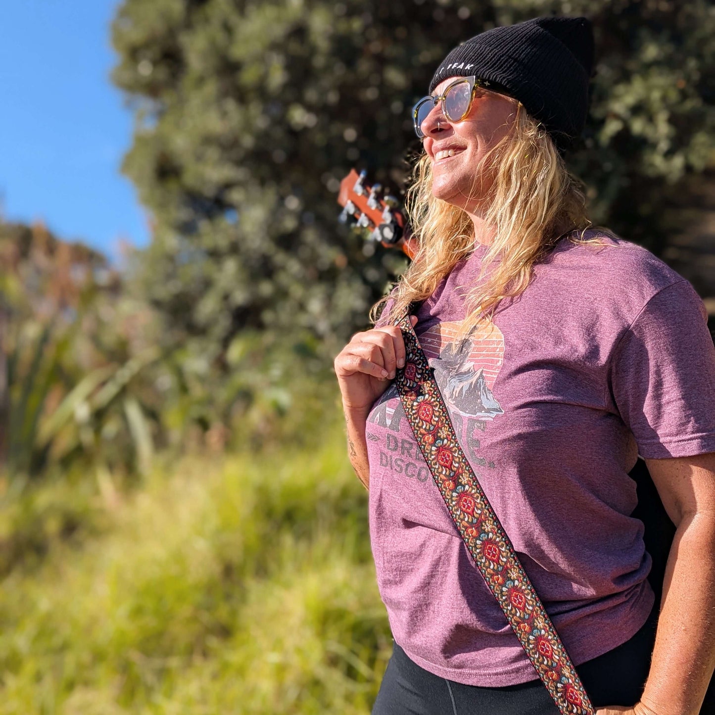 Front view of Sim Bastick in Wyld Peak Explorers eco tee with guitar at Matauri Bay NZ