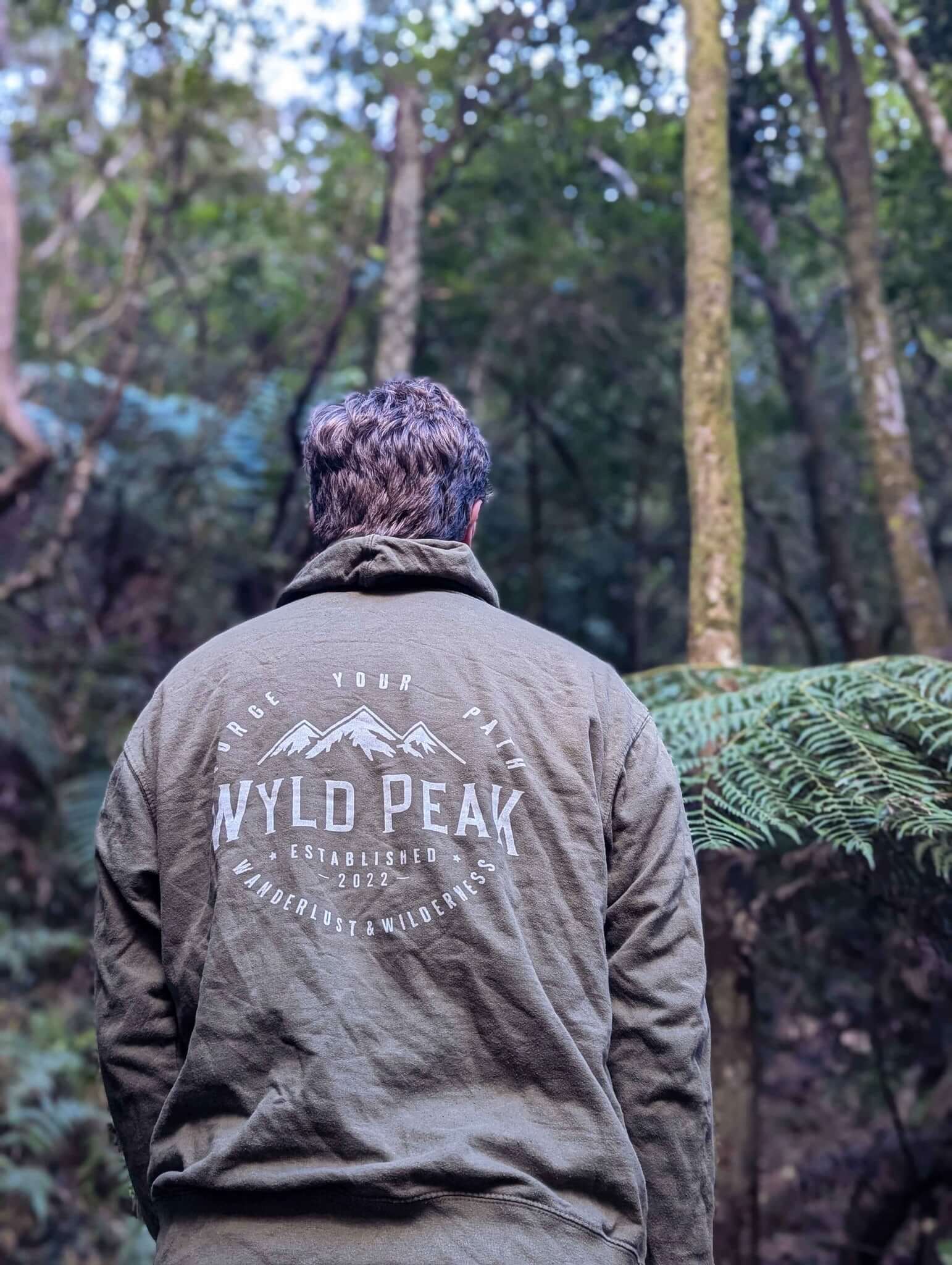 Backshot of Alexander hiking on a forest trail wearing a Wyld Peak classic hoodie.