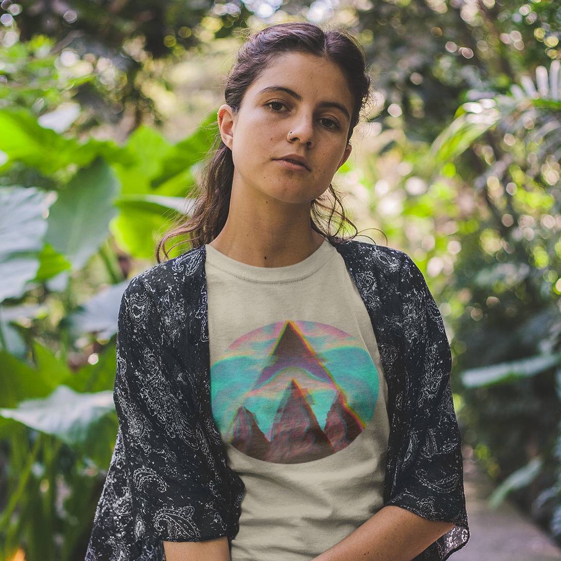 A woman wearing a beige organic cotton t-shirt with a geometric mountain design, paired with a black cardigan, standing outdoors.