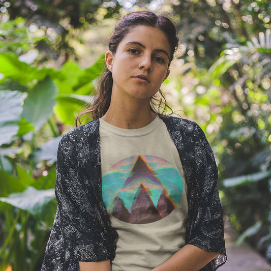 A woman wearing a beige organic cotton t-shirt with a geometric mountain design, paired with a black cardigan, standing outdoors.